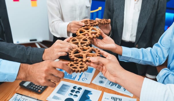 Office worker holding cog wheel as unity and system teamwork in corporate workplace with piles of business paper and financial report on meeting table. Business people with business success. Concord