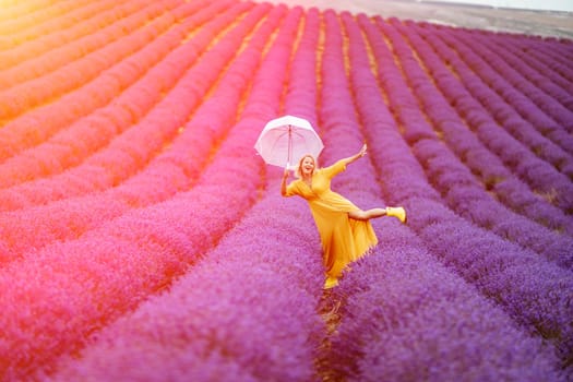 A middle-aged woman in a lavender field walks under an umbrella on a rainy day and enjoys aromatherapy. Aromatherapy concept, lavender oil, photo session in lavender.