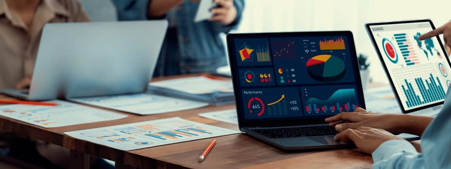 Panorama shot analyst team utilizing BI Fintech to analyze financial report with laptop. Businesspeople analyzing BI power dashboard displayed on laptop screen for business insight. Scrutinize