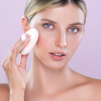 Closeup alluring beautiful female model applying powder puff for facial makeup concept. Portrait of flawless perfect cosmetic skin woman put powder foundation on her face in pink isolated background.