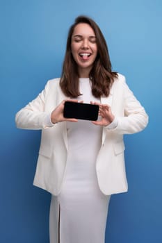 smiling young brunette with long hair woman in white dress showing smartphone screen with mockup.