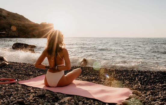 Young woman in swimsuit with long hair practicing stretching outdoors on yoga mat by the sea on a sunny day. Women's yoga fitness pilates routine. Healthy lifestyle, harmony and meditation concept.