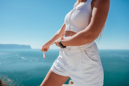 a young and slender woman in shorts holds in her hand a measuring yellow tape on her sexy thighs on the beach. concept of detox and diet