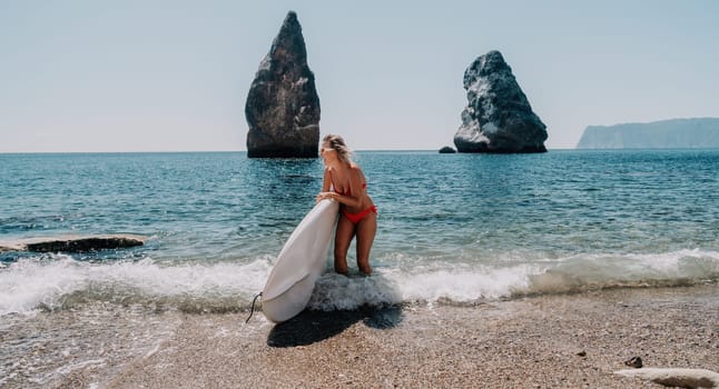 Close up shot of beautiful young caucasian woman with black hair and freckles looking at camera and smiling. Cute woman portrait in a pink bikini posing on a volcanic rock high above the sea