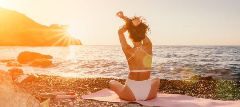 Young woman in swimsuit with long hair practicing stretching outdoors on yoga mat by the sea on a sunny day. Women's yoga fitness pilates routine. Healthy lifestyle, harmony and meditation concept.