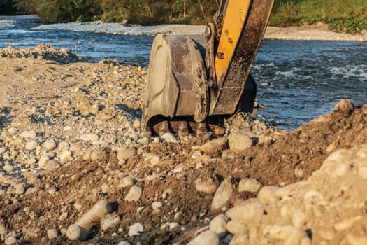 Excavator (digging machine) bucket digging ground by the river.