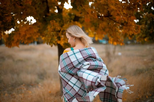 autumn woman in a green dress, plaid, against the background of an autumn tree.