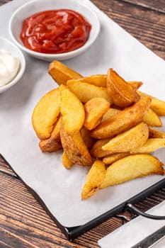 Potato wedges with ketchup and mayonnaise on wooden table