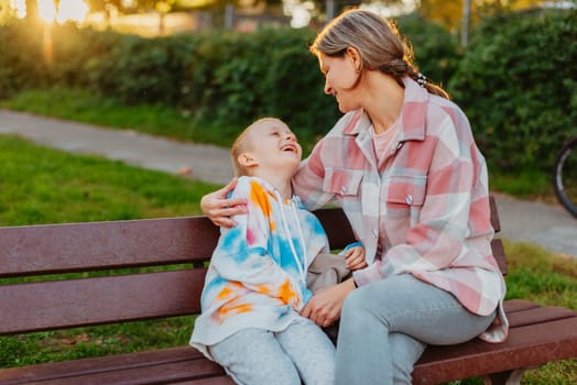 mother and son sit on a park bench in the rays of the setting sun. the concept of a family. Mother's Day. beautiful girl (mother) with a boy (son) in the park in the park are sitting on a bench at sunset.