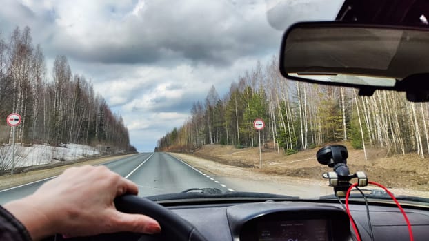 Photo with partial focus with a view from the car from the driver's seat to nature, the road, the sky with clouds. A woman's hand on the steering wheel on journey