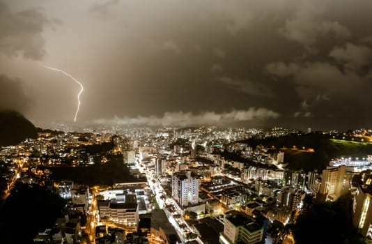 A thunderbolt strikes the city on a dark night with yellow lights and space for text, surrounded by towering architecture.