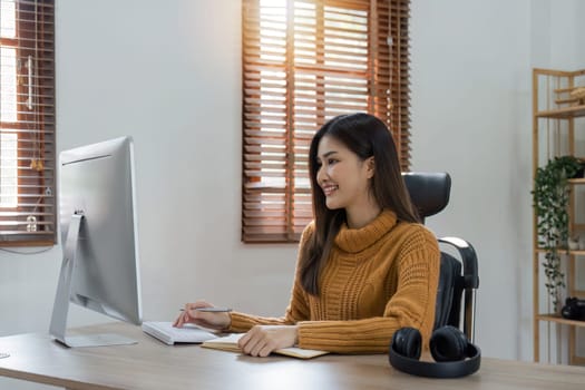 Young woman sits at table and looks at computer working at home.