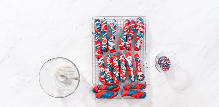 Flat lay. Drizzling white glaze on top of patriotic cinnamon twists. and decorating with star sprinkles.