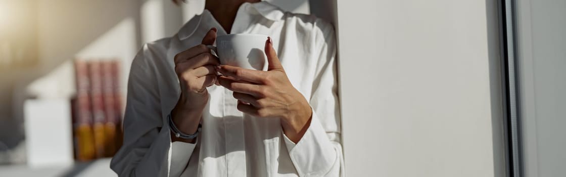 Close up of business woman holding cup of coffee and standing near window. Blurred background