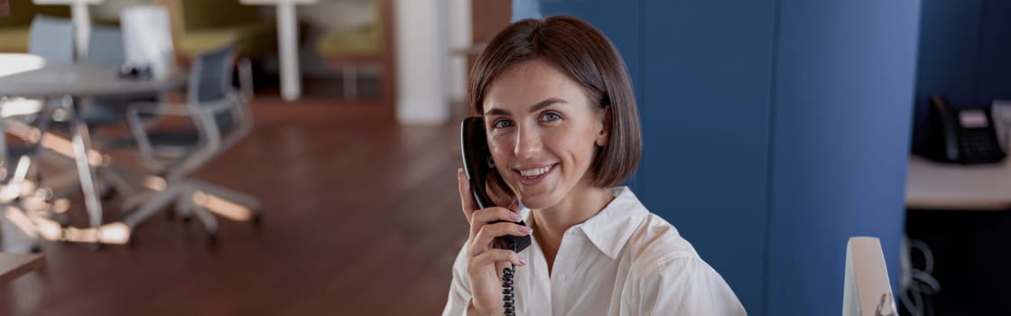 Smiling woman worker talk phone with client sit on her workplace in office. Blurred background