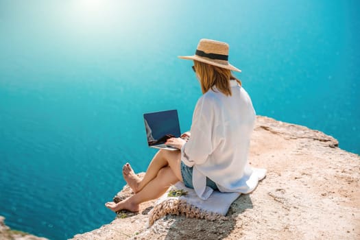 Freelance woman working on a laptop by the sea, typing away on the keyboard while enjoying the beautiful view, highlighting the idea of remote work