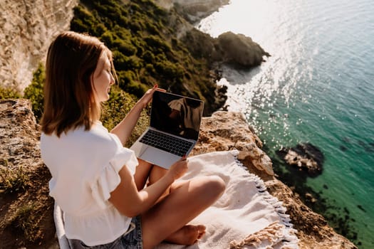 Freelance woman working on a laptop by the sea, typing away on the keyboard while enjoying the beautiful view, highlighting the idea of remote work