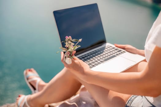 Freelance woman working on a laptop by the sea, typing away on the keyboard while enjoying the beautiful view, highlighting the idea of remote work