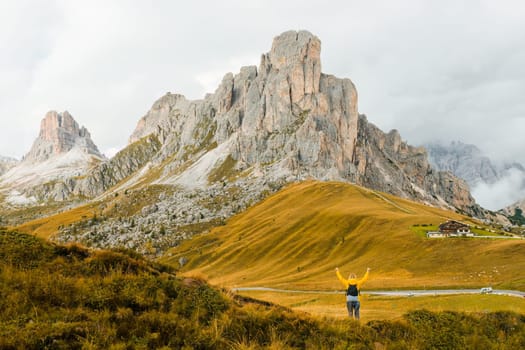 Hiker reaching hands to sky enjoys exploring mountain nature on Pass Giau. Female tourist looks around and enjoys vacation on high mountain range