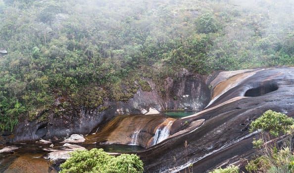A misty environment surrounds the river as it has created colorful holes in the wall over time, creating beautiful natural pools.