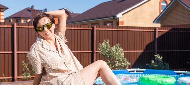 Portrait of pretty young woman in pajama sitting near inflatable swimming pool - summer and country life