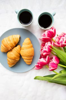 croissants on the background of laces with a bouquet of pink tulips, happy morning.