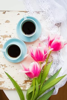 two cups of coffee and pink tulips on an old table.