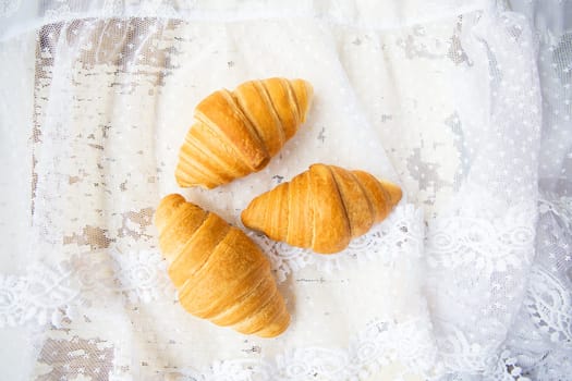 Beautiful and delicious croissants on the background of old laces and white table.