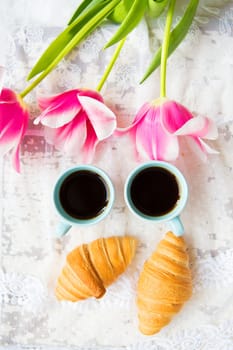 nice cup of coffee, croissants and pink tulips on old white table, close-up.