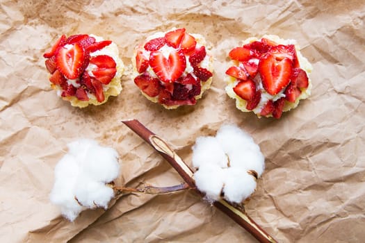 Beautiful cupcakes with strawberries along with a branch of cotton lies on kraft paper.