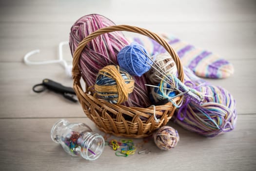 Colored threads, knitting needles and other items for hand knitting, on a light wooden table .