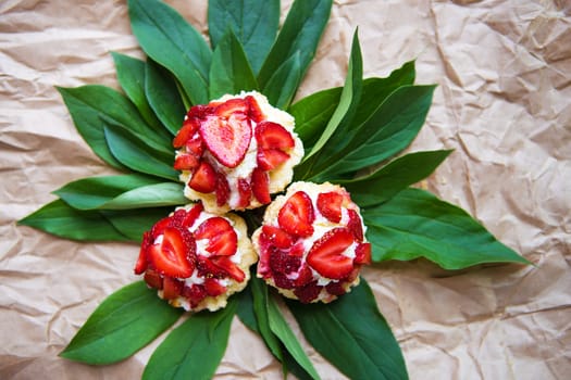 Beautiful and bright cupcakes with strawberries lie on green leaves, close-up.