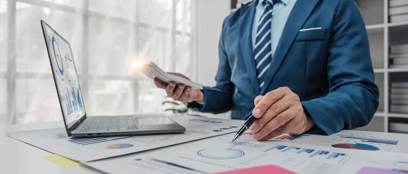 Close up Businessman using calculator and laptop for do math finance on wooden desk in office and business working background, tax, accounting, statistics and analytic research concept