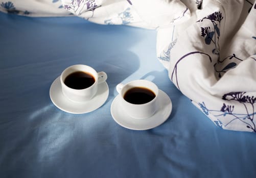 Two white cups of coffee are in bed, sunny morning.
