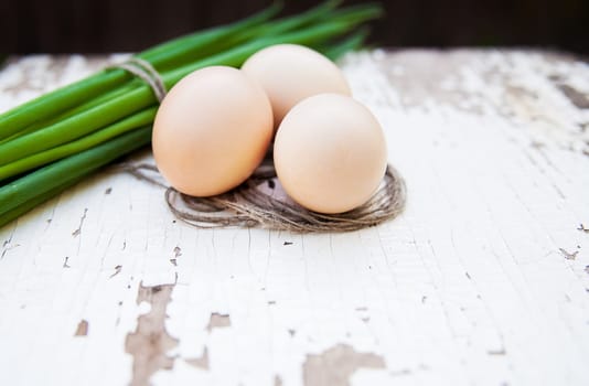 Spring onions and eggs lie on an old white table