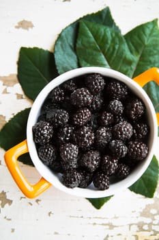 A full blackberry plate stands on an old wooden background, close-up.