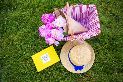 Beautiful flowers in a basket and yellow album lie on the grass-bright picnic