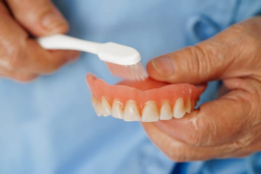 Asian senior woman patient holding teeth denture in her hand for chew food.