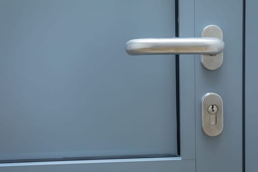Gray aluminum door with steel-colored metal handle and lock cylinder installed. Close-up view of selected components.