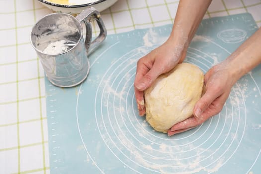 A woman kneads the dough with her hands, the hands of a baker, a silicone mat, a sieve, handmade baking. View from above