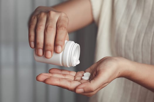 Asian woman's hand pouring medicines from a white bottle for medical and healthcare concept.