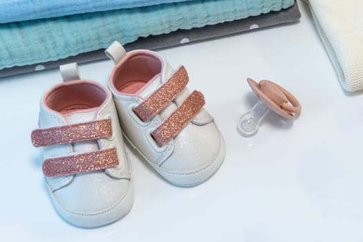 Baby girl pink shoes with other newborn baby accessories on white surface