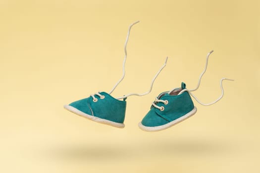 Flying baby shoes with flying laces on yellow background. Newborn baby concept with levitation