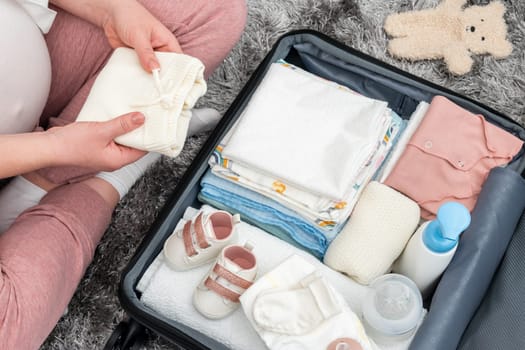 Pregnant woman packing baby clothing in suitcase