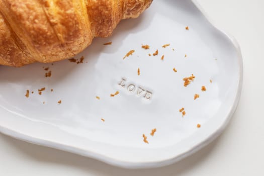 White handmade clay plate with fresh croissant on a white table