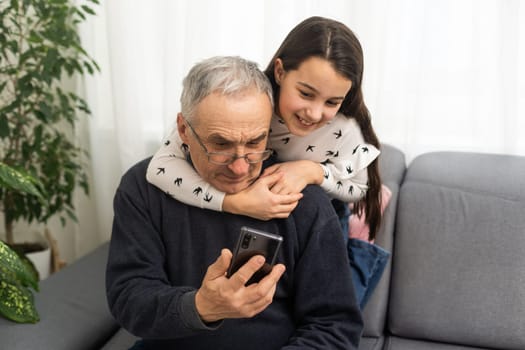 Senior man 60-65 years old showing his little granddaughter how to use a smartphone.