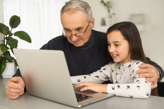 Portrait of grandfather and granddaughter doing homework with laptop