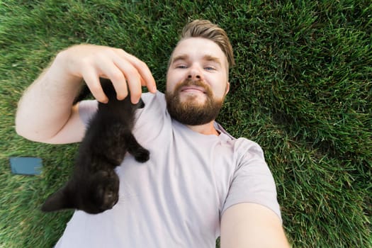 Man with little kitten lying and playing on grass - friendship love animals and pet owner