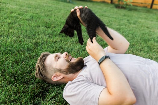 Man with little kitten lying and playing on grass - friendship love animals and pet owner