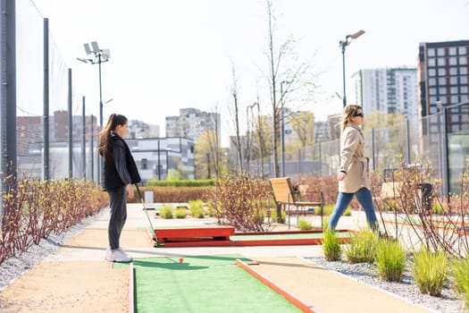 Mother playing with her cute daughter in mini golf.